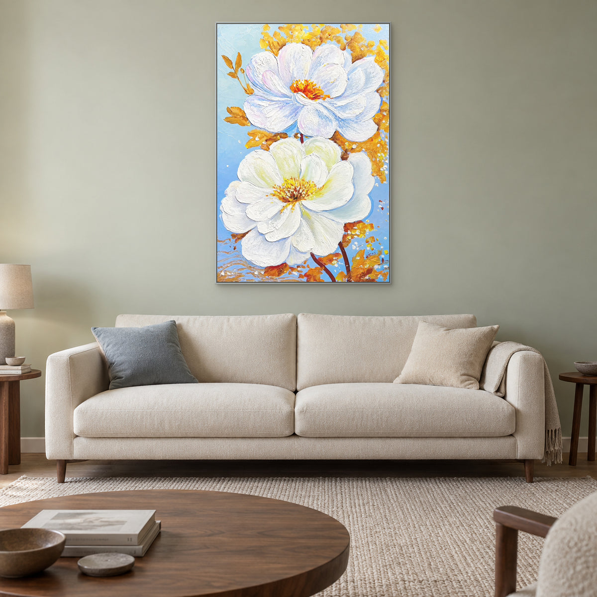 Vertical white and gold floral painting in a silver-coloured floating frame above a cream sofa on a muted green wall.