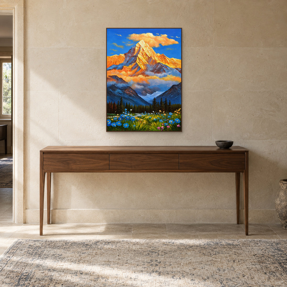 Wildflower mountain landscape in a walnut-tone frame above a wooden console against a pale stone wall