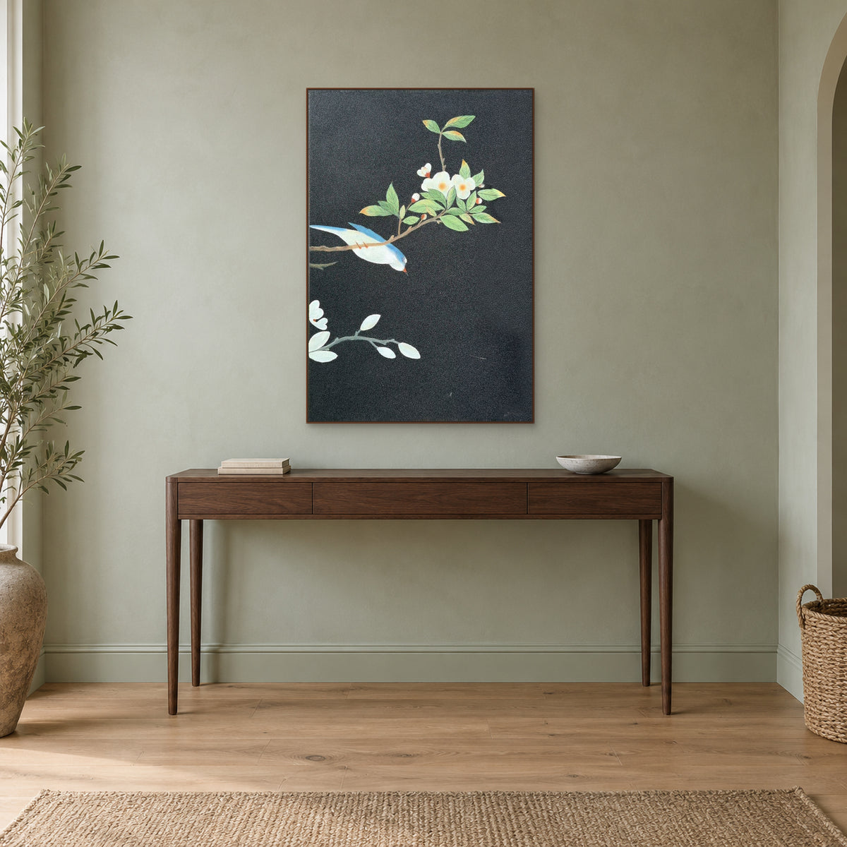 White blossoms and blue bird in a walnut-tone frame above a slim wooden console on a sage wall