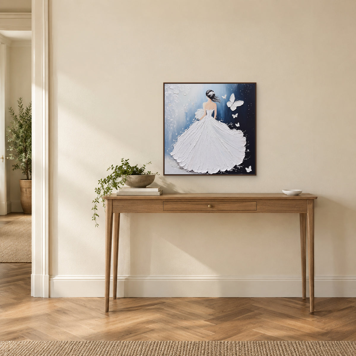 White gown and butterflies in a dark wood-tone frame above a narrow console on a warm ivory entryway wall