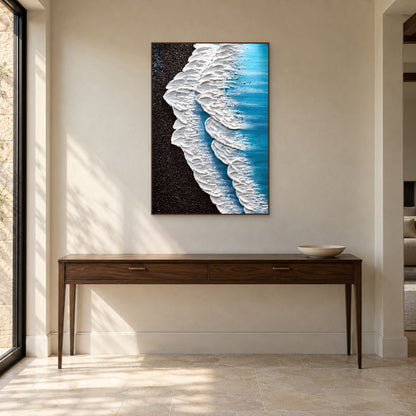 White surf and dark shoreline artwork in a walnut-tone frame above a console with a shallow bowl