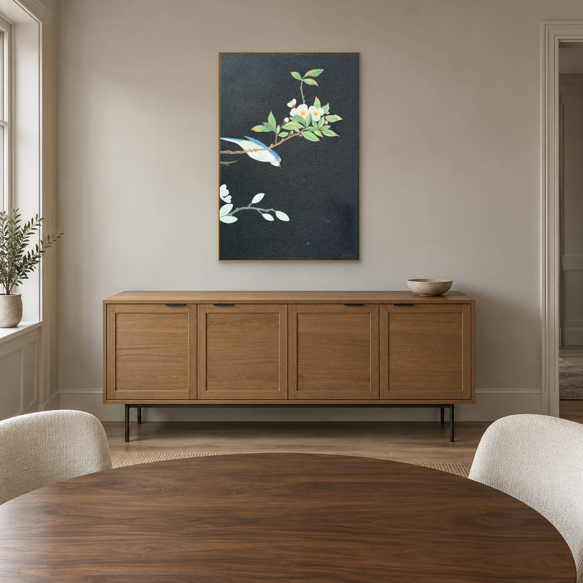 Champagne-framed bird and floral painting above an oak-tone sideboard behind a round dining table