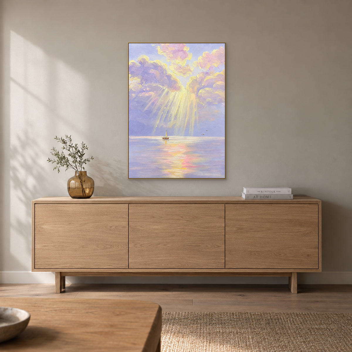 Pastel seascape in a champagne-tone frame above a pale wooden sideboard with a small amber vase and books.