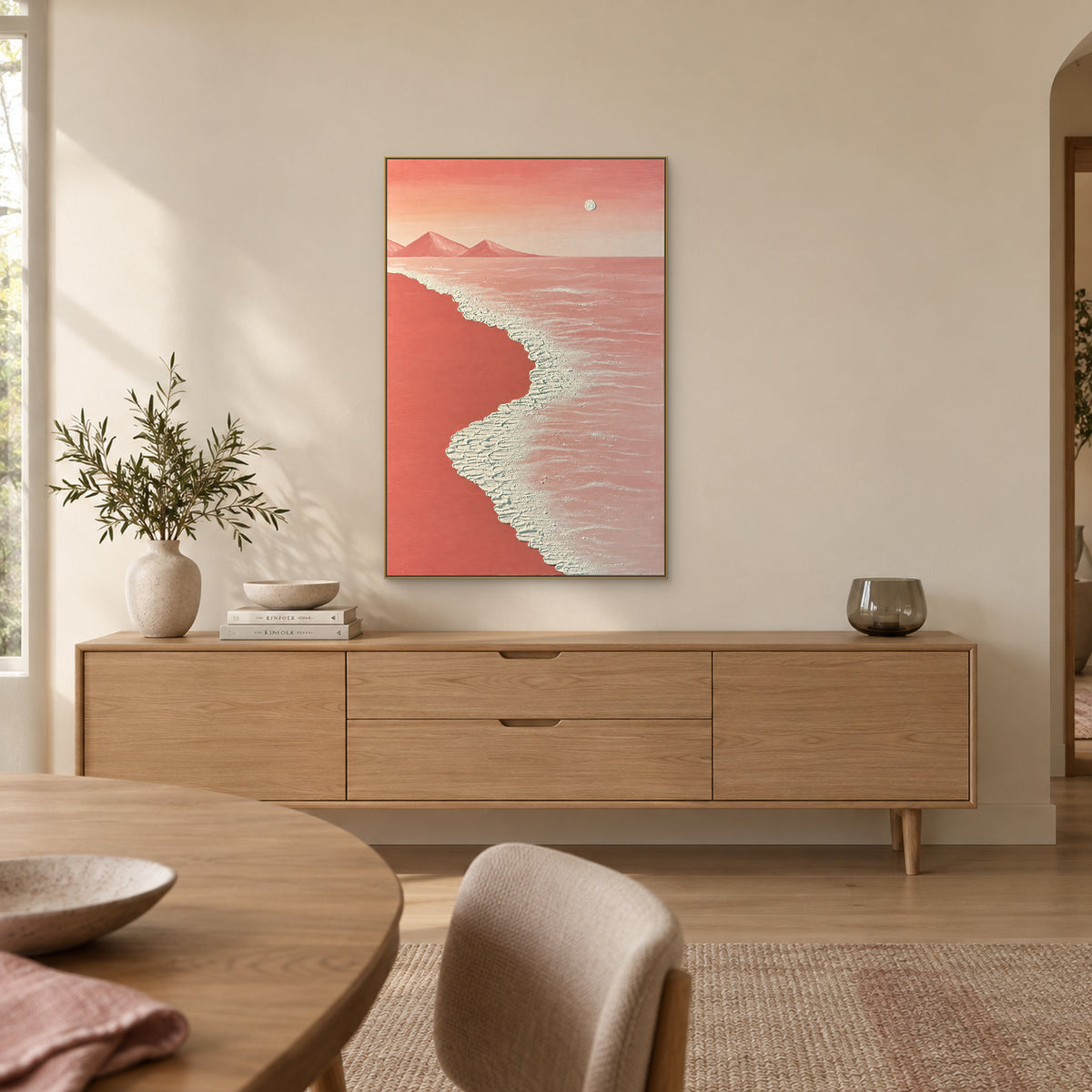 Pink coastal painting in a champagne-tone floating frame above a wooden dining-room sideboard