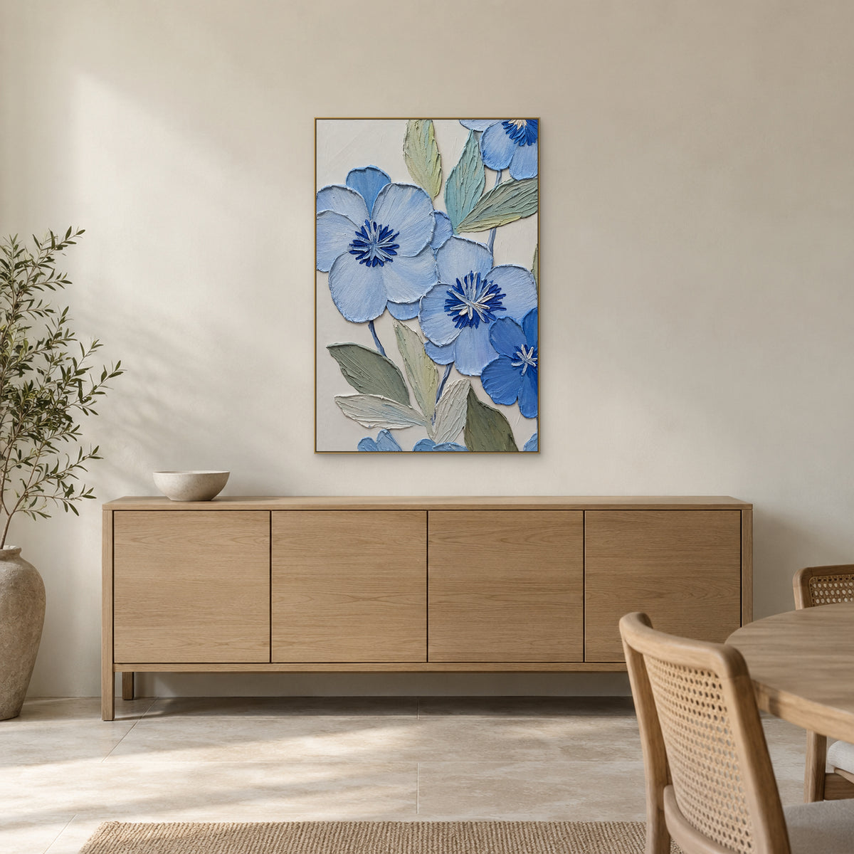 Blue flowers and sage foliage in a champagne-tone frame above a pale wood dining-room sideboard