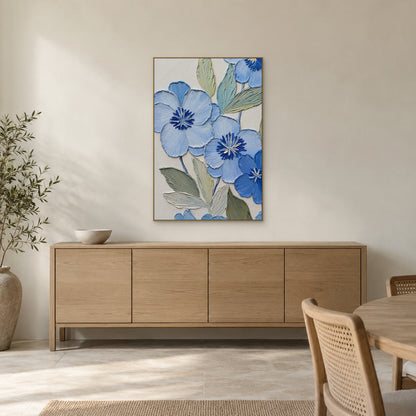 Blue flowers and sage foliage in a champagne-tone frame above a pale wood dining-room sideboard