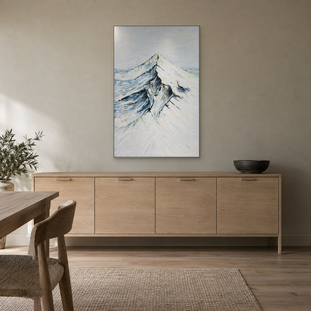 Snowy mountain painting in a champagne-tone frame above a pale wood dining room sideboard