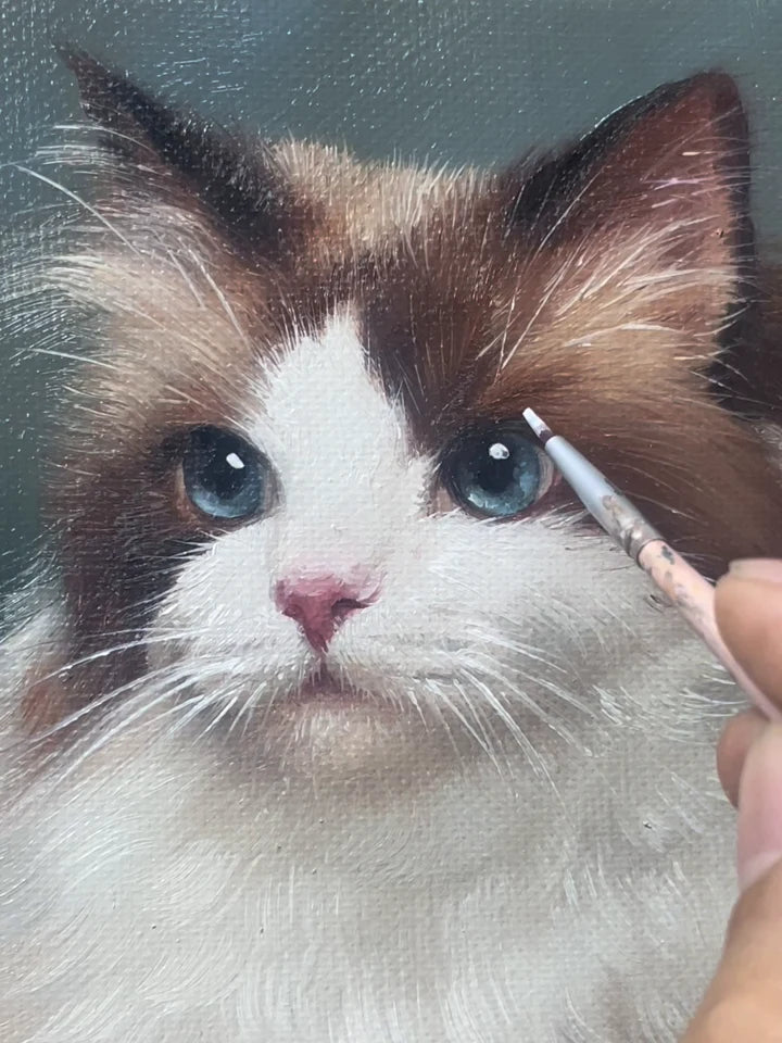 Un pinceau ajoute de fins détails autour de l’œil bleu d’un portrait de chat peint à la main