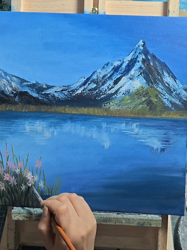 Un artiste peint des fleurs au bord d’un lac alpin bleu dans un paysage de montagne