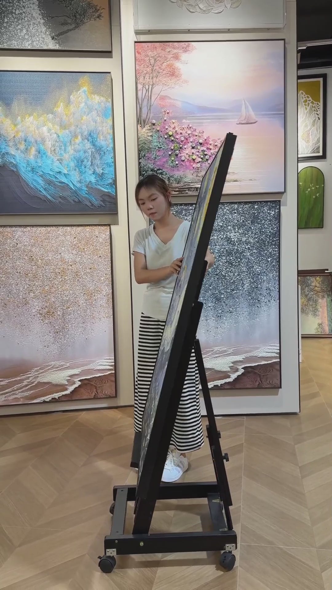 A person turns the blue and yellow starry village painting from its edge towards a full front view in a gallery.