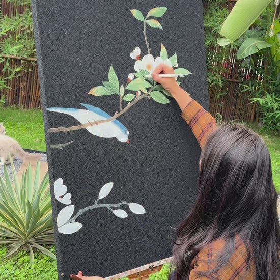 Two painting-process views of a blue bird and flowering branches on a dark canvas