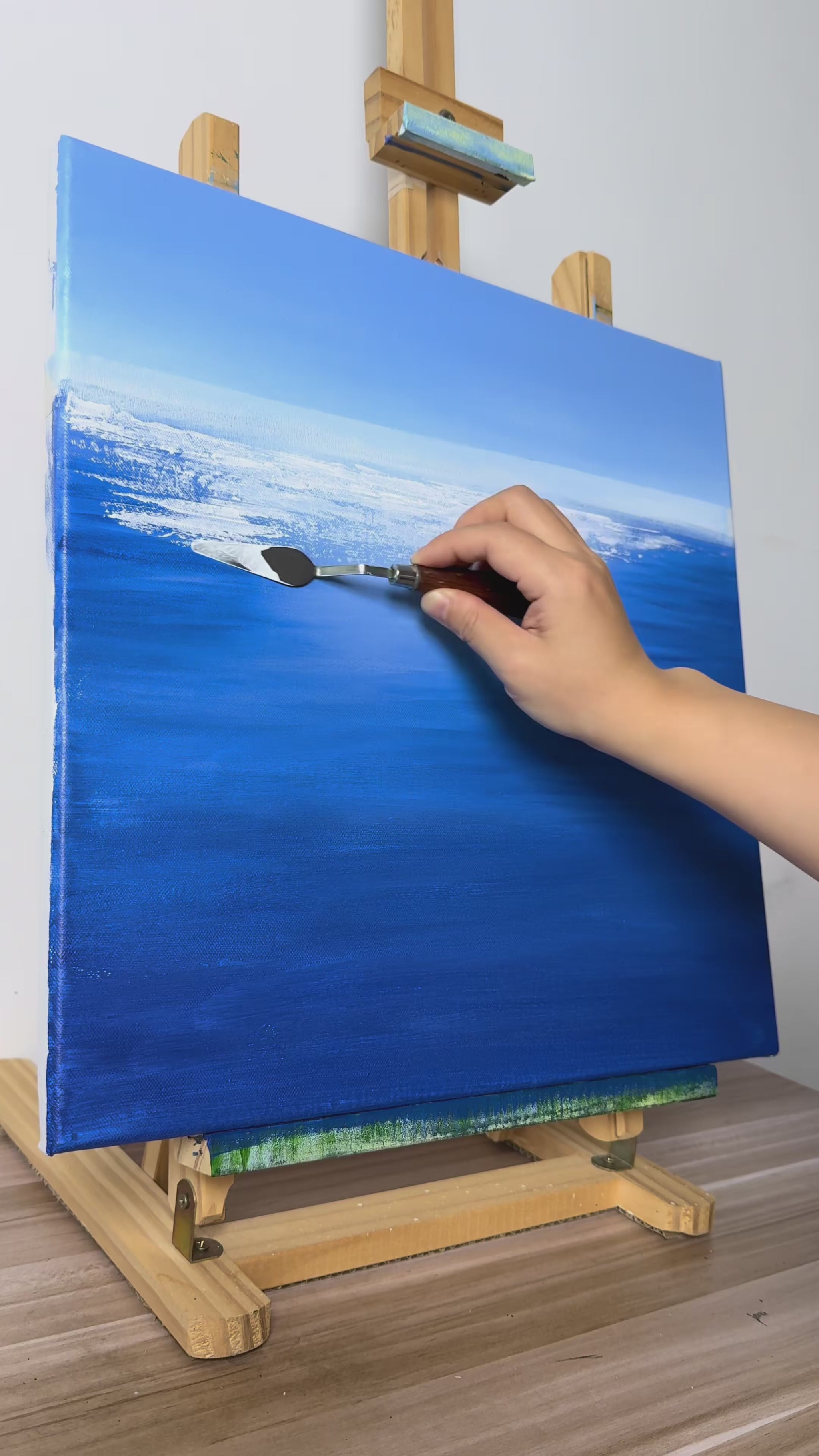 Hand-painting white water reflections and green grasses, followed by the finished blue seascape on an easel