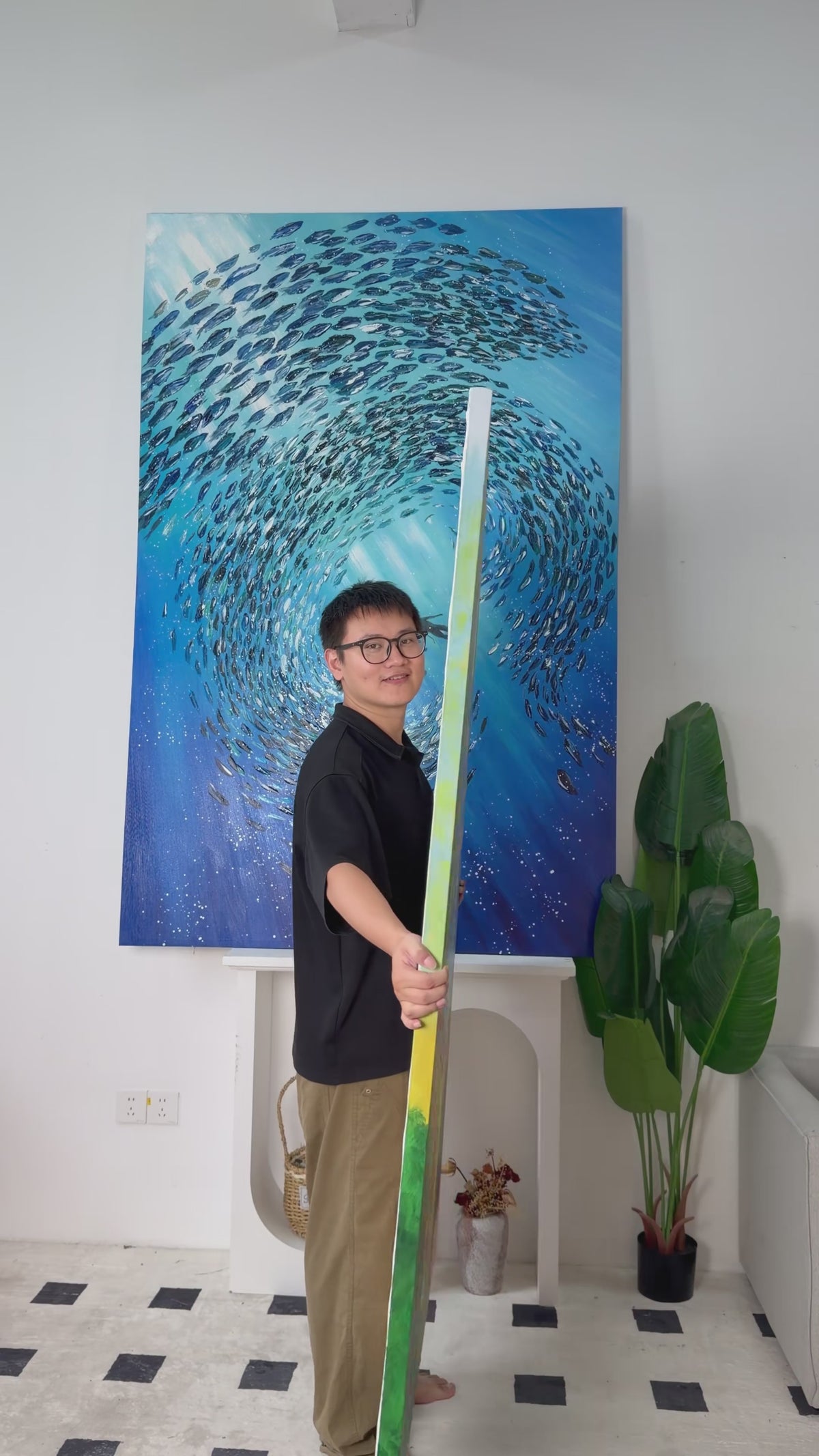 Studio video turning the tall painting from its side to reveal a blue lake, pink flowers, yellow-green trees and a small bear